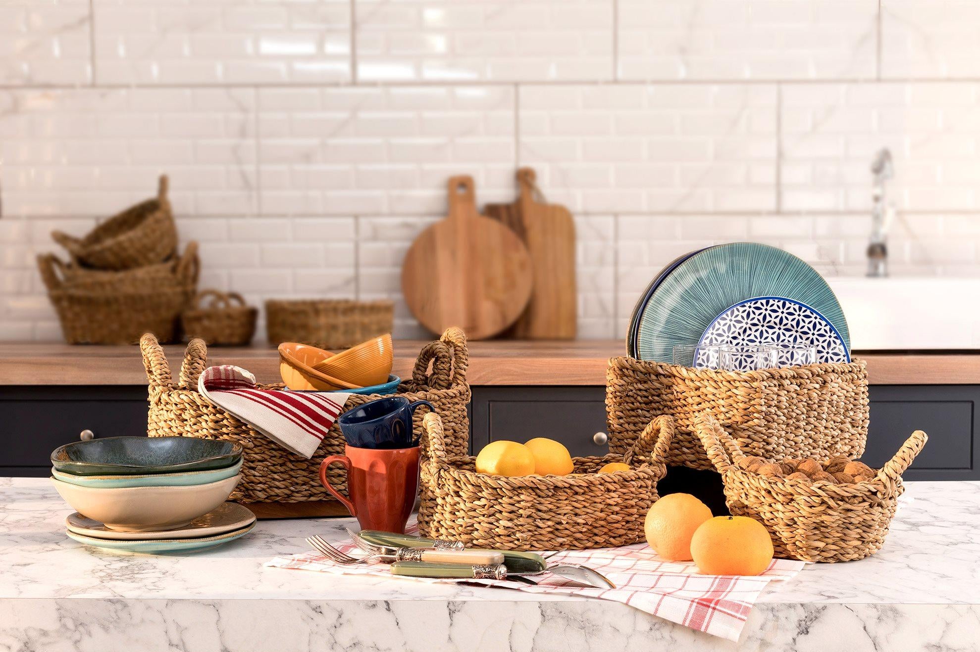 Kitchen counter with wicker baskets, bowls, mugs, and oranges on a marble countertop.